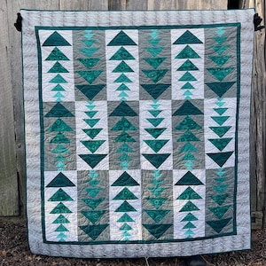 May include: A green and grey quilt with a geometric pattern of triangles. The quilt is made up of multiple squares, each with a different arrangement of triangles. The quilt is quilted with a simple stitch pattern.