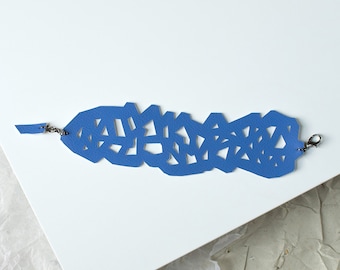 May include: A blue leather bracelet with a geometric cut-out design. The bracelet has two silver clasps.