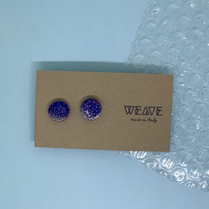 以下が含まれることがあります： 白い斑点のある小さな丸い青いイヤリングのペア。イヤリングは、「WEAVE made in Italy」というテキストが書かれた茶色のカードの上にあります。