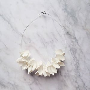 Könnte beinhalten: Weiße Halskette aus Stoffblumen. Die Halskette liegt auf einem weißen Marmoruntergrund.