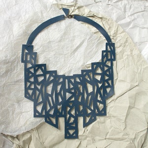 May include: A dark blue leather necklace with a geometric design. The necklace is made of multiple layers of leather that have been cut out to create a pattern of triangles and squares.