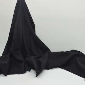 May include: A black, soft, and lightweight scarf with a fringed edge. The scarf is draped over a white surface.