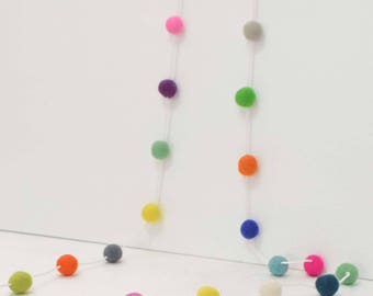 Puede incluir: Una guirnalda colorida de bolas de fieltro enhebradas en una cuerda blanca. La guirnalda presenta una variedad de colores, incluyendo rojo, naranja, amarillo, verde, azul, morado y rosa.