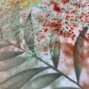 May include: Close-up of a fabric with a floral pattern. The design features green, brown, and yellow botanical elements. The fabric has a textured appearance, with visible details of leaves and small dotted accents.