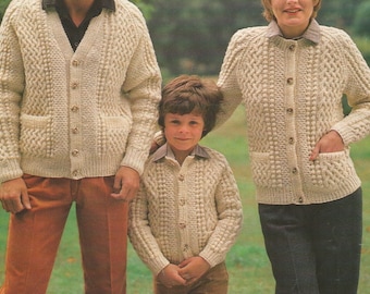 May include: A family wearing matching cream-colored knit cardigans with button closures and front pockets. The cardigans have a textured pattern. The child is wearing a collared shirt. The adults are wearing collared shirts and pants.