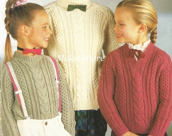 May include: Three children wearing knitted sweaters with cable knit patterns. The sweaters are in cream, green, and pink. The children are smiling and looking at each other.
