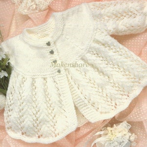 May include: White knitted baby cardigan with a delicate lace pattern and heart-shaped buttons. The cardigan has a scalloped hem and is made with a soft yarn.