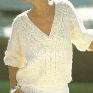 May include: A white knitted sweater with a v-neck and cable knit detail. The sweater has a relaxed fit and is made with a soft yarn.