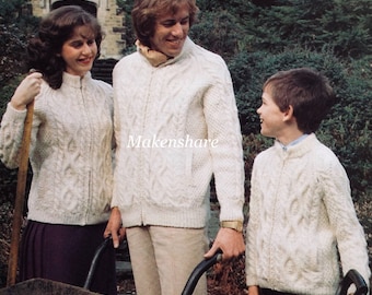 May include: A family of three wearing white cable knit sweaters with zipper closures. The sweaters have a diamond pattern. The family is standing in a garden setting.