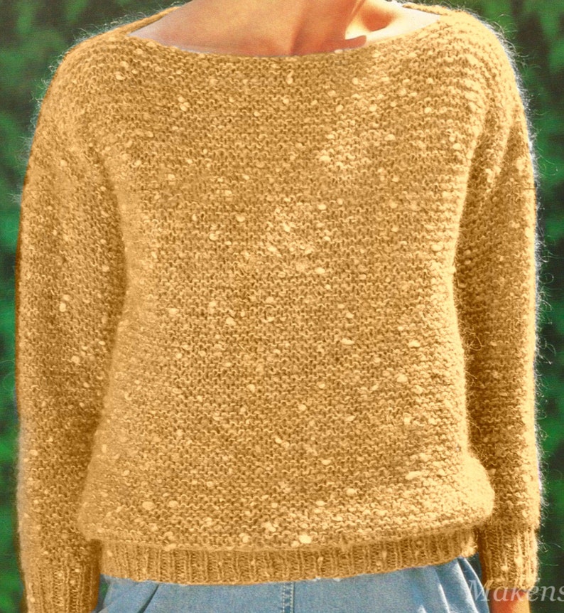 May include: A mustard-colored knit sweater with a wide neckline. The sweater has a textured appearance with small, lighter-colored flecks throughout the fabric. The cuffs and hem are ribbed, and the overall style is casual and comfortable.