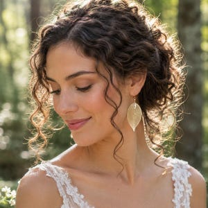 May include: A gold-toned earring shaped like a delicate, skeletonised leaf with a fine, intricate vein structure. The earring hangs from a simple hook, featuring a metallic finish that catches the light, creating a subtle, shimmering appearance.