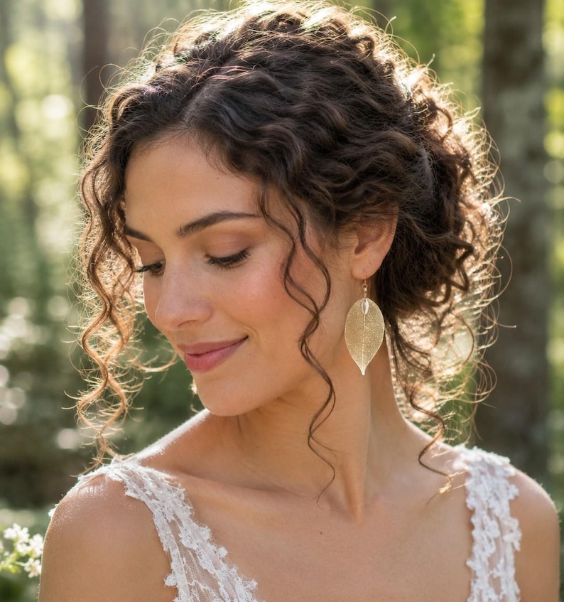 May include: A gold-toned earring shaped like a delicate, skeletonised leaf with a fine, intricate vein structure. The earring hangs from a simple hook, featuring a metallic finish that catches the light, creating a subtle, shimmering appearance.
