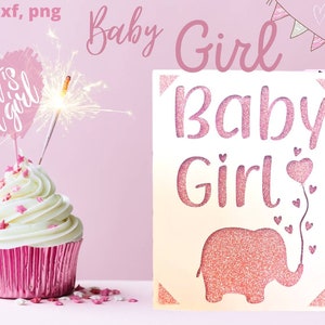 Puede incluir: Un cupcake rosa y blanco con chispas rosas y una parte superior en forma de coraz&oacute;n rosa que dice "It's a girl" con una chispa en la parte superior. Un letrero blanco con letras de brillo rosa dice "Baby Girl" con un elefante de brillo rosa y corazones rosas.
