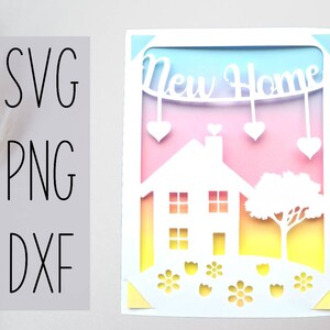 Pode incluir: Um cart&atilde;o branco com um design recortado de uma casa, uma &aacute;rvore, flores e uma faixa que diz "New Home". O fundo &eacute; um degradado de rosa, amarelo e azul.