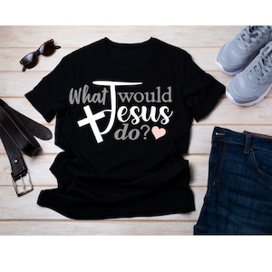 Pode incluir: Camiseta preta com o texto "What would Jesus do?" em branco com uma cruz e um coração rosa.