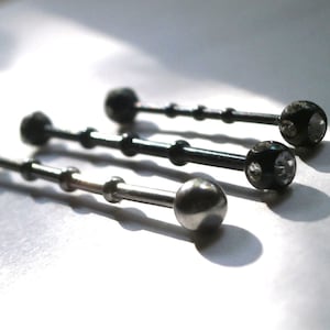 May include: Three silver barbell style body jewellery pieces with clear gem accents. The top two pieces are black with clear gems. The bottom piece is silver with a smooth ball end.