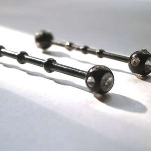 May include: Two black barbell style body piercings with clear crystal accents.