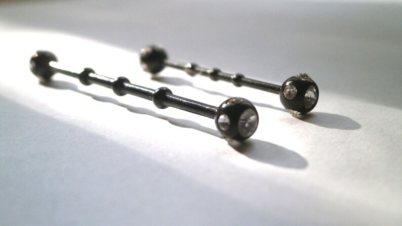 May include: Two black barbell style body piercings with clear crystal accents.