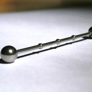 May include: A silver barbell with two round balls on either end. The barbell has a smooth, polished finish.