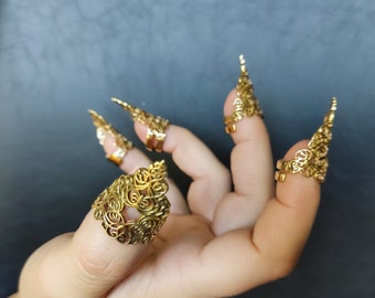 Puede incluir: Conjunto de cinco anillos de dedo dorados con intrincados diseños florales. Los anillos están diseñados para ajustarse sobre la uña y tienen una punta puntiaguda.