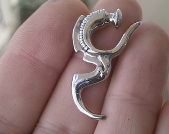 Op de afbeelding: Zilverkleurig metalen body piercing in de vorm van een gestileerde draak. De piercing is bedoeld om in het oor te worden gedragen.