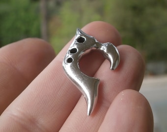 Op de afbeelding: Een zilverkleurige metalen hanger met een uniek, abstract ontwerp. De hanger heeft een gebogen vorm met een gat aan de bovenkant om een ​​ketting of koord aan te bevestigen.