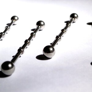 May include: Four silver barbell body jewellery pieces with ball ends. The barbells are arranged in a row on a white surface.