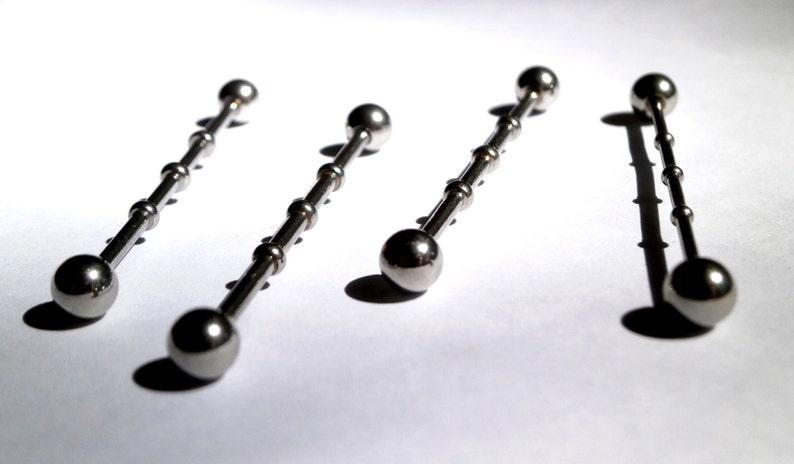 May include: Four silver barbell body jewellery pieces with ball ends. The barbells are arranged in a row on a white surface.