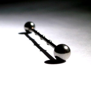 May include: A silver barbell with two round balls on either end. The barbell is lying on a white surface.