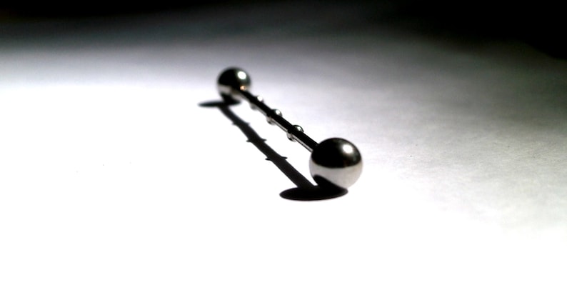 May include: A silver barbell with two round balls on either end. The barbell is lying on a white surface.