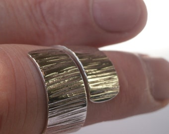 May include: A silver ring with a textured, hammered finish. The ring is designed to wrap around the finger.
