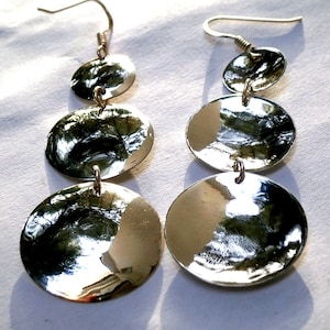 May include: Silver dangle earrings with three round discs, each with a hammered texture. The discs are graduated in size, with the largest disc at the bottom.