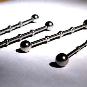 May include: Four silver barbell body jewellery pieces with ball ends. The barbells are different lengths.