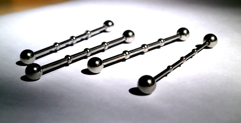 May include: Four silver barbell body jewellery pieces with ball ends. The barbells are different lengths.