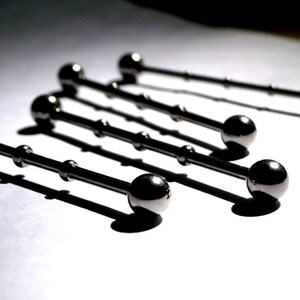 May include: Five silver barbell piercings with ball ends. The barbells are arranged in a staggered pattern on a white surface.