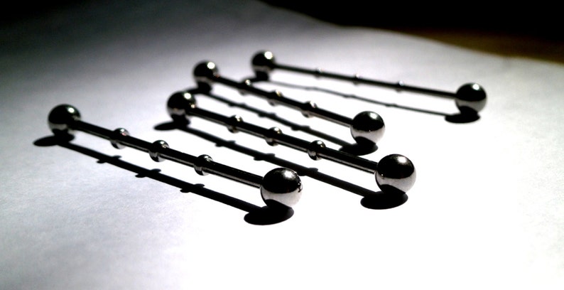 May include: Five silver barbell piercings with ball ends. The barbells are arranged in a staggered pattern on a white surface.