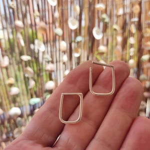 May include: A pair of small, open-ended rectangular earrings crafted from a smooth, polished metallic material. Each earring features a continuous, rounded-corner frame design that remains open at one end, showcasing a simple and clean geometric aesthetic.
