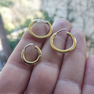 May include: Three gold hoop earrings of different sizes. The earrings are shown on a hand.