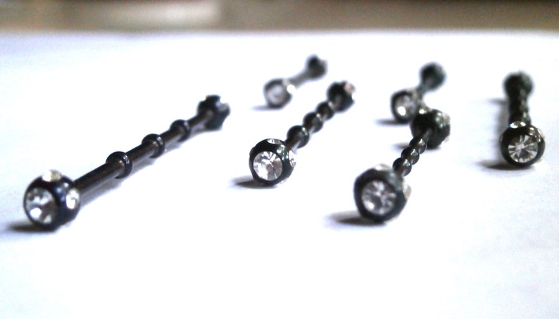 May include: Five black barbell body jewellery pieces with clear crystal accents.