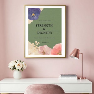 Könnte beinhalten: Ein gerahmter Wandkunstdruck mit einem salbeigrünen Hintergrund, einem violetten Stiefmütterchen oben und rosa Blüten unten. Der Text lautet: She is clothed with STRENGTH & DIGNITY; she can laugh at the days to come. PROVERBS 31:25.