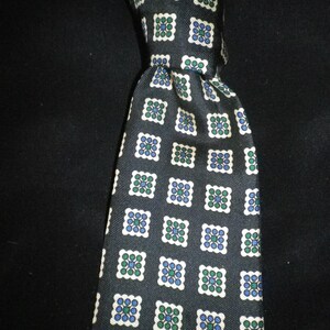 May include: A dark navy tie featuring a repeating pattern of white-edged squares. Each square is filled with a design of green and blue circles. The tie is knotted, highlighting the fabric's texture and pattern. A classic accessory for formal wear.