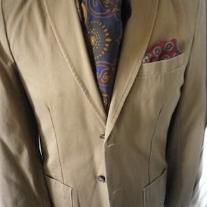 May include: A tan blazer with a paisley patterned scarf and a red pocket square.