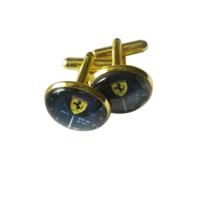 May include: A pair of gold cufflinks with a black and yellow Ferrari logo on each cufflink.