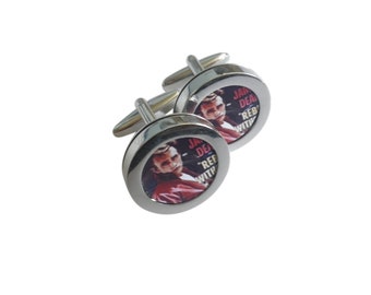 May include: A pair of silver cufflinks with a round, black and white image of a man's face and the text "Don't Deal With The Rebel Without A Cause".