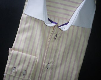 May include: A light yellow and pink striped dress shirt with a white collar and purple trim. The shirt has a button-down collar and a single button cuff.