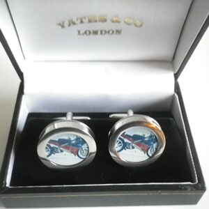 Puede incluir: Un par de gemelos de plata con una imagen de motocicleta dentro de un marco redondo. Los gemelos están en una caja negra con interior blanco y el texto "Yates & Co London" en la tapa.