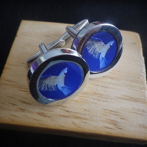 May include: A pair of silver cufflinks with a blue background and a white bird design.