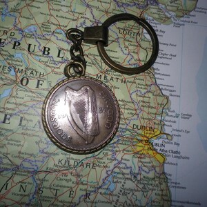 May include: A bronze key chain with a round coin charm featuring a harp and the words "ÉIRE" and "SAORSTAT ÉIREANN". The coin charm is on a map of Ireland.