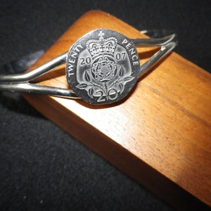 May include: A silver bangle bracelet with a 20 pence coin from 2007 featuring a rose and the words "TWENTY PENCE" on it.
