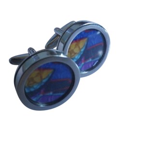 May include: A pair of silver cufflinks with a round, blue, purple and yellow patterned design.